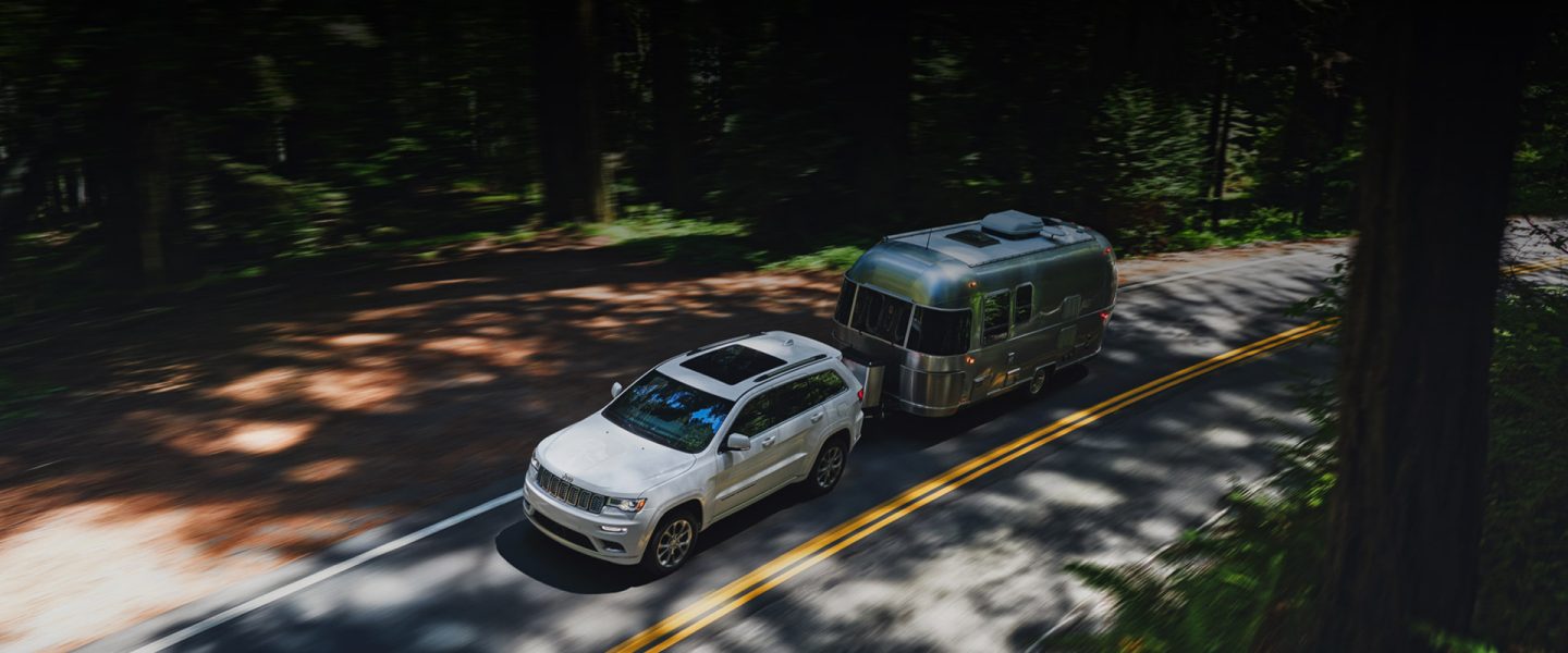 A 2020 Jeep Grand Cherokee towing a trailer on a curving road.