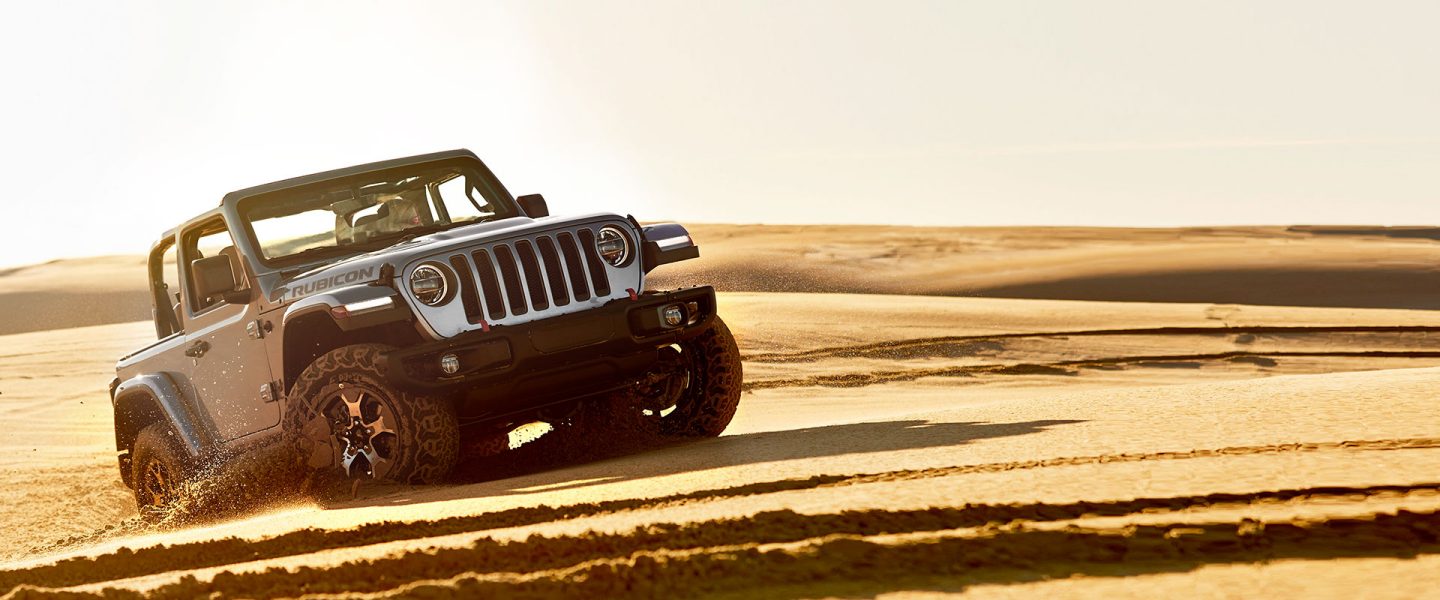 A 2020 Jeep Wrangler Rubicon with its top off, being driven on sand.