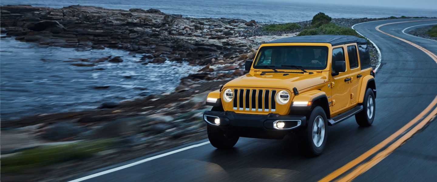 A 2020 Jeep Wrangler being driven on a winding road by the water.