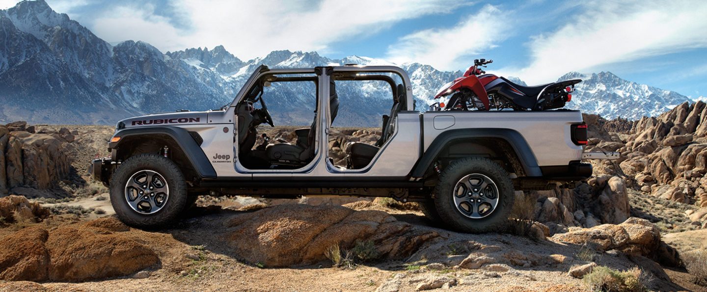 The 2021 Jeep Gladiator Rubicon parked on a mountain with its doors off and an ATV in its truck bed.