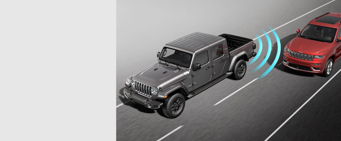 The 2021 Jeep Gladiator Overland with illustrated sensors monitoring the area behind the rear bumper, detecting a vehicle in the next lane.