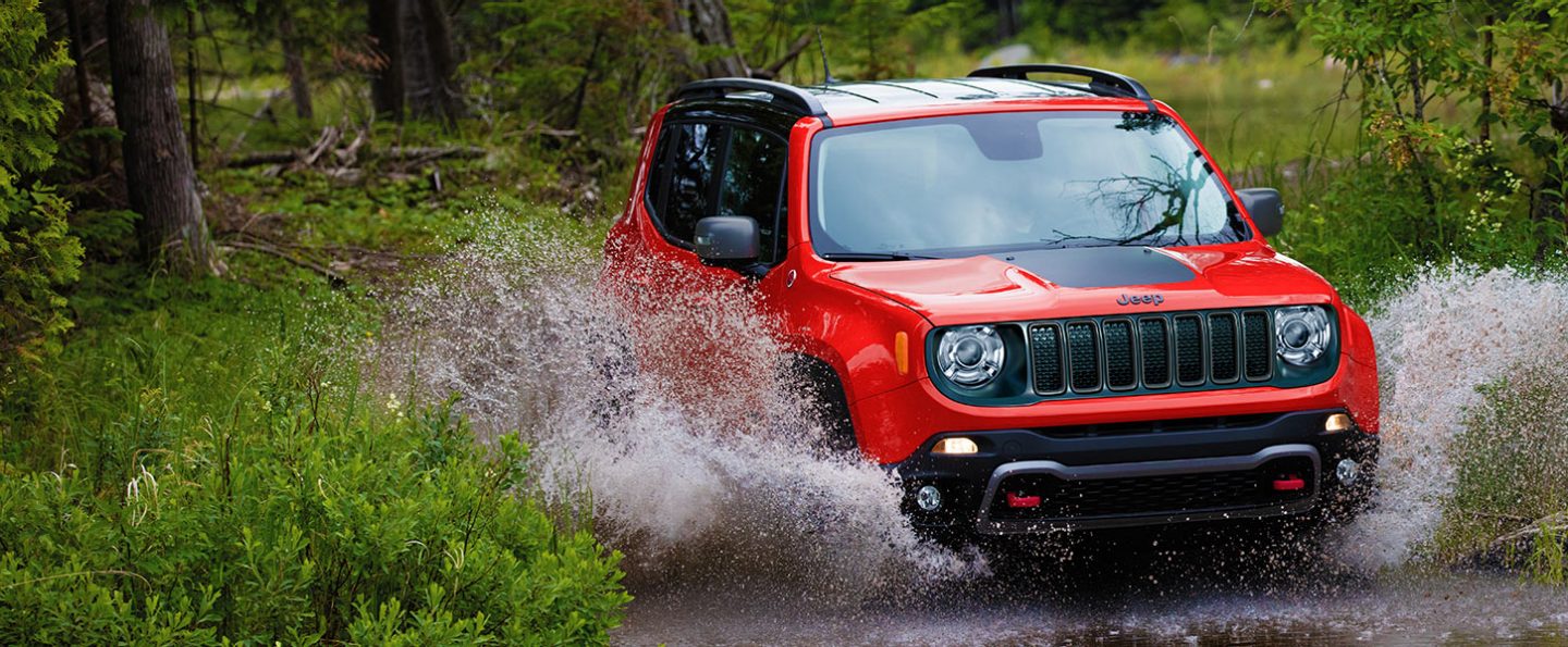 A red 2021 Jeep Renegade making a splash as it fords a stream.