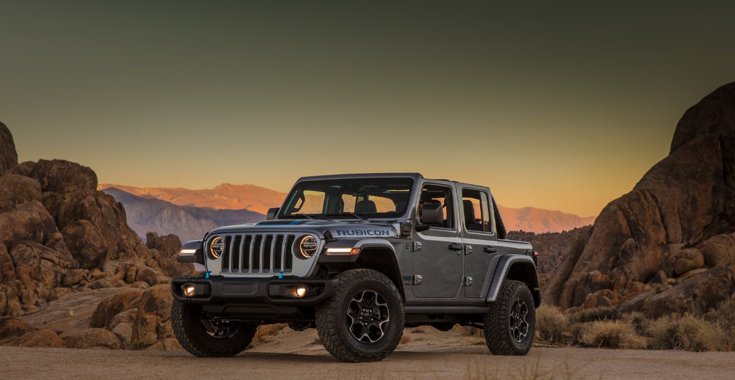 Three-quarter side view of a 2021 Jeep Wrangler 4xe parked on a trail in the mountains at dusk.