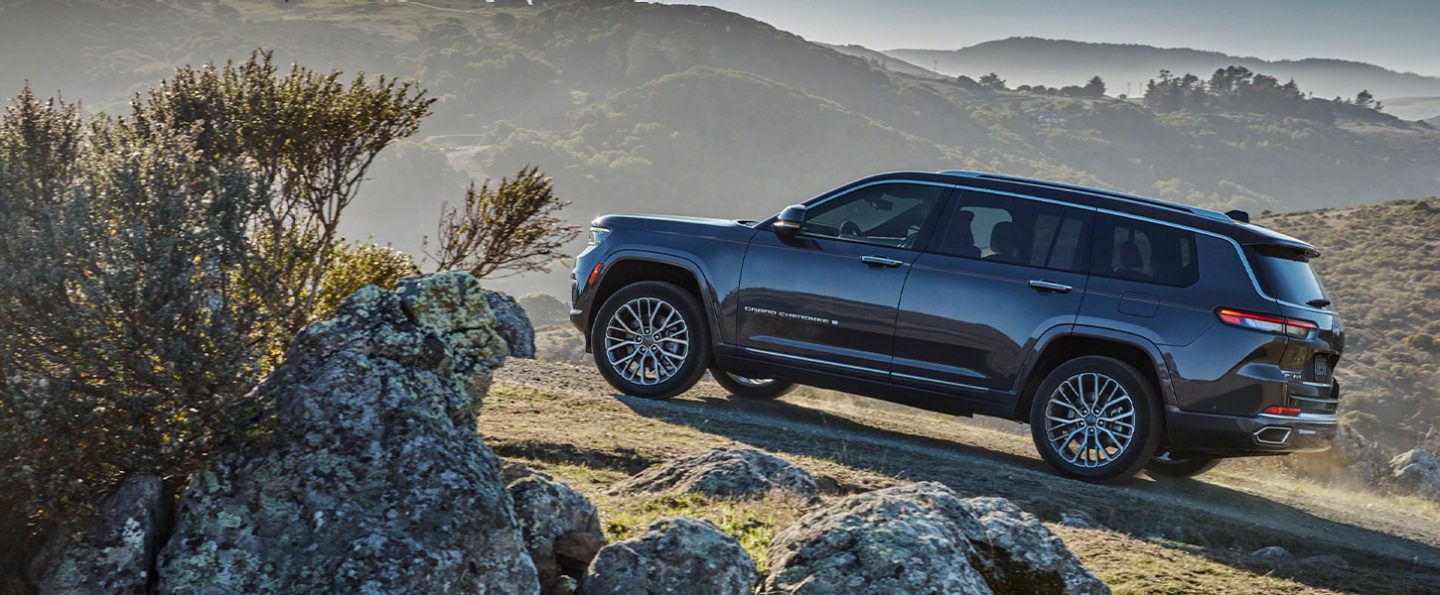 The 2021 Jeep Grand Cherokee L Summit Reserve parked facing uphill on a grassy track in the mountains.